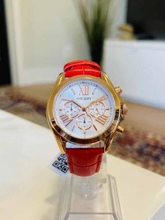 Gold watch with a red strap on a stand in a blurred indoor setting